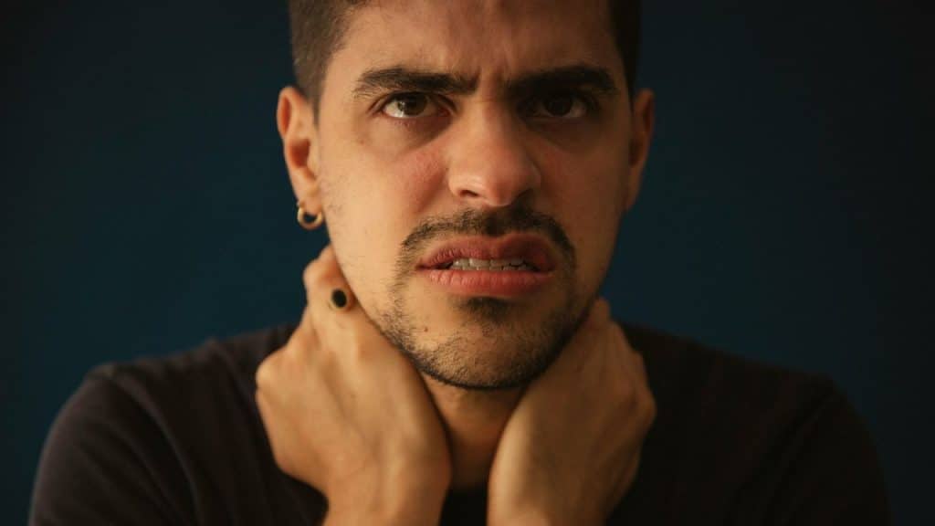 A man with a pained expression and hands on his neck.