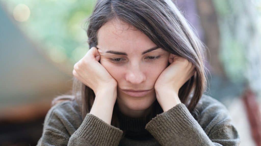 A young woman with a sad expression, resting her face on her hands.