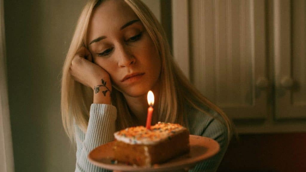 A disappointed woman with a tattoo on her wrist looks at a piece of cake with a candle.