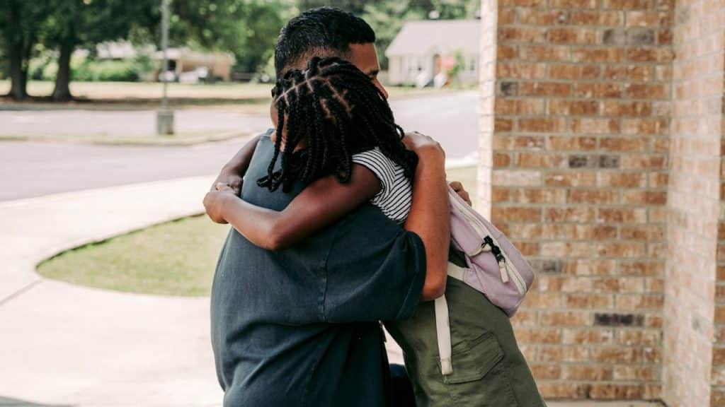 A dad and his young daughter with braided hair share a warm hug.