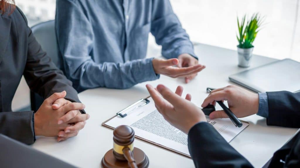 An unrecognizable couple sits with a lawyer at a table with legal papers and a gavel.
