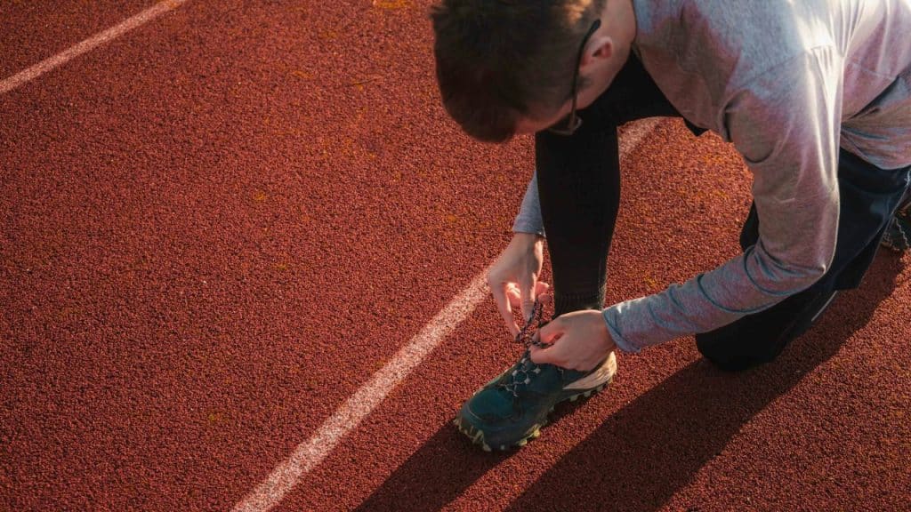 A male runner kneels on a red track to tie his sneaker.