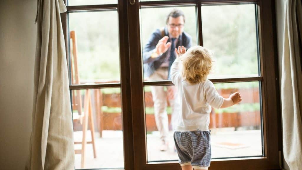 A child waves at his father through a glass door.