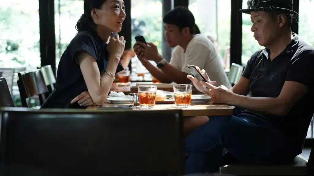 A woman talks with a men at a restaurant table looking at his phones.