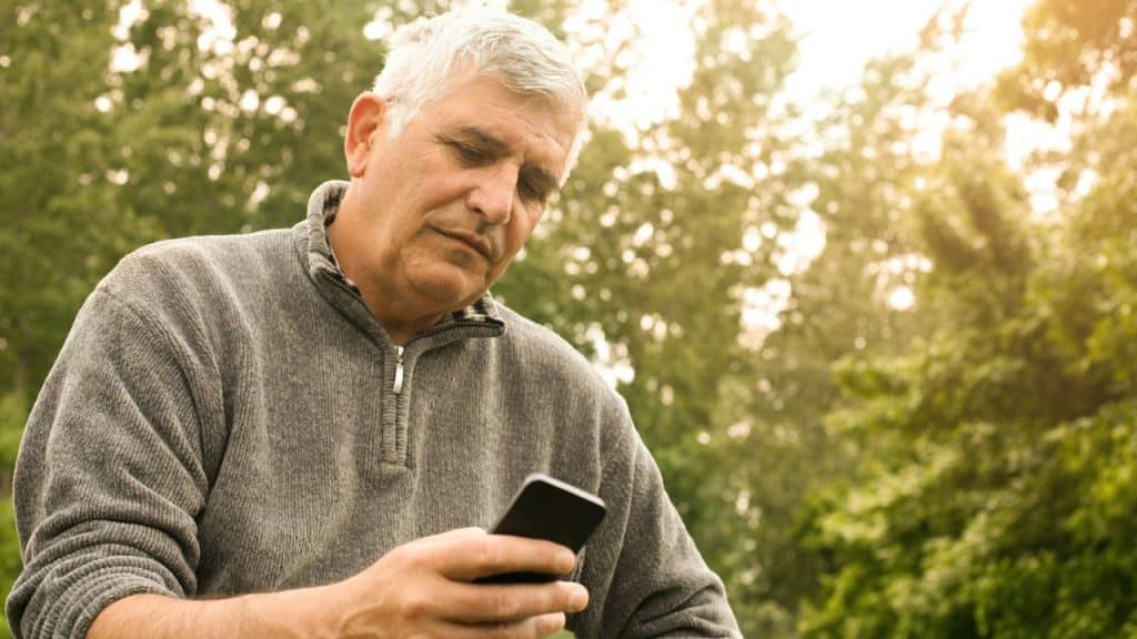 A mature man in a gray sweater looks at a cell phone.