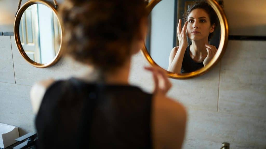 A woman looking at herself in a bathroom mirror.