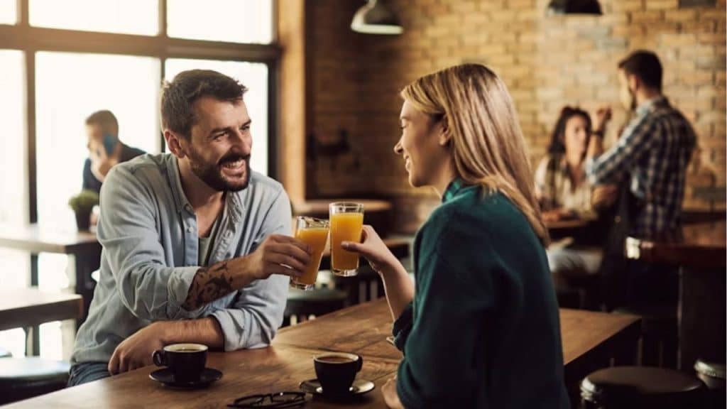 Man and a woman happily toasting with orange juice in a restaurant