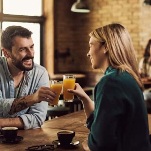 Man and a woman happily toasting with orange juice in a restaurant