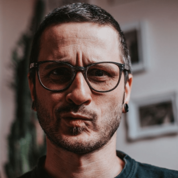 A serious man with glasses and a beard is looking at the camera.