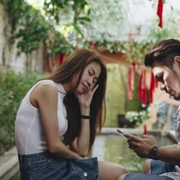 Couple at the park looking bored while the man is scrolling on his phone