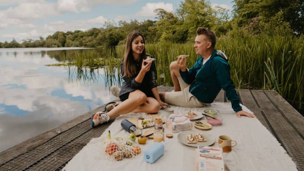 Couple having a picnic with fruit and wraps by a lake