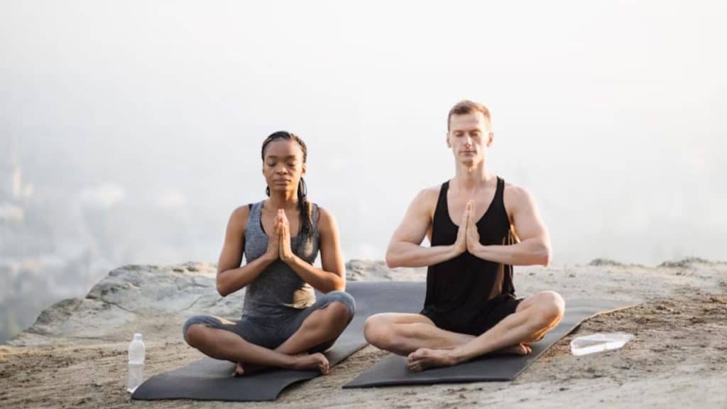 Couple meditating together on yoga mats at sunset