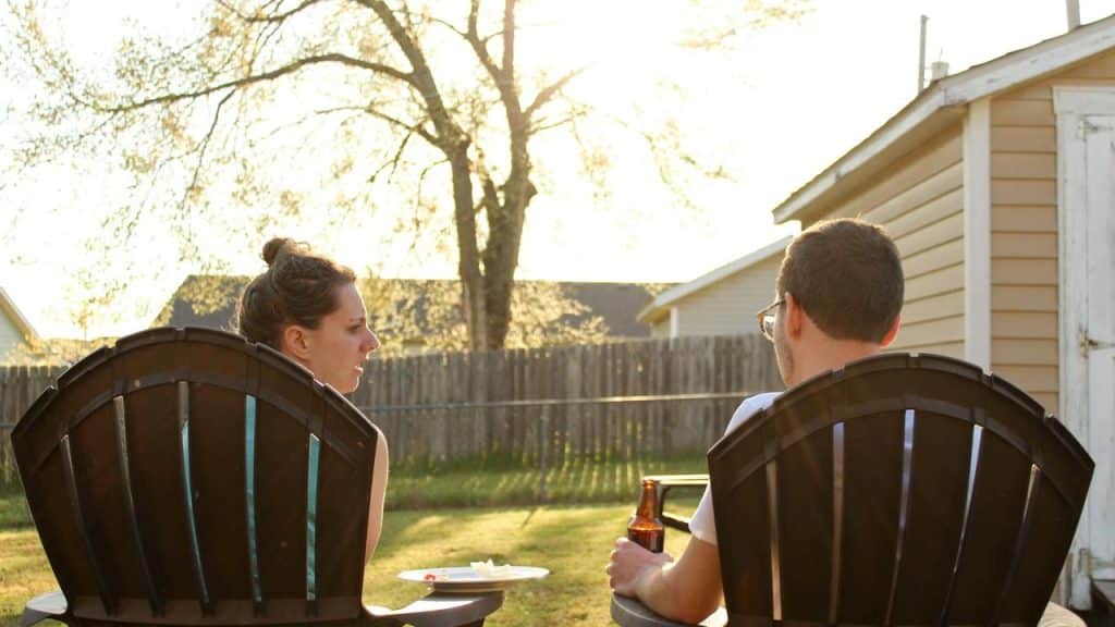 A man and woman sitting in chairs outside, talking in the evening sunlight.