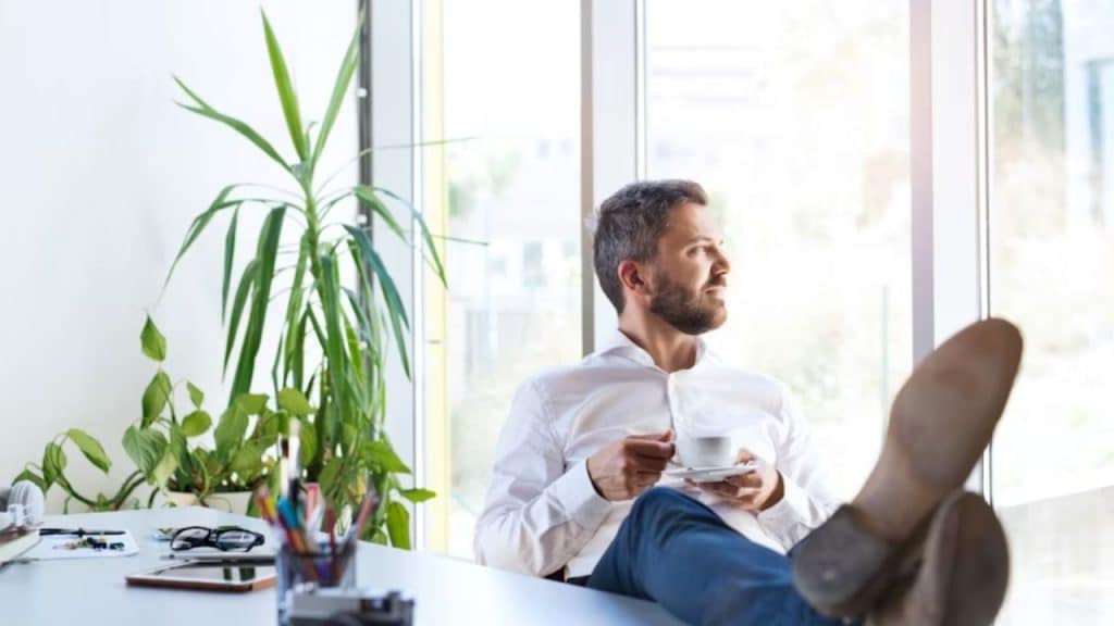 Man sitting confidently with feet on the table drinking coffee and reflecting on himself