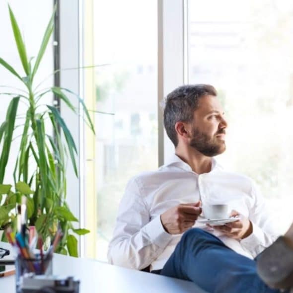 Man sitting confidently with feet on the table drinking coffee and reflecting on himself