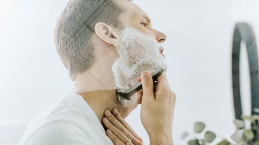 A man carefully shaves his beard at home.