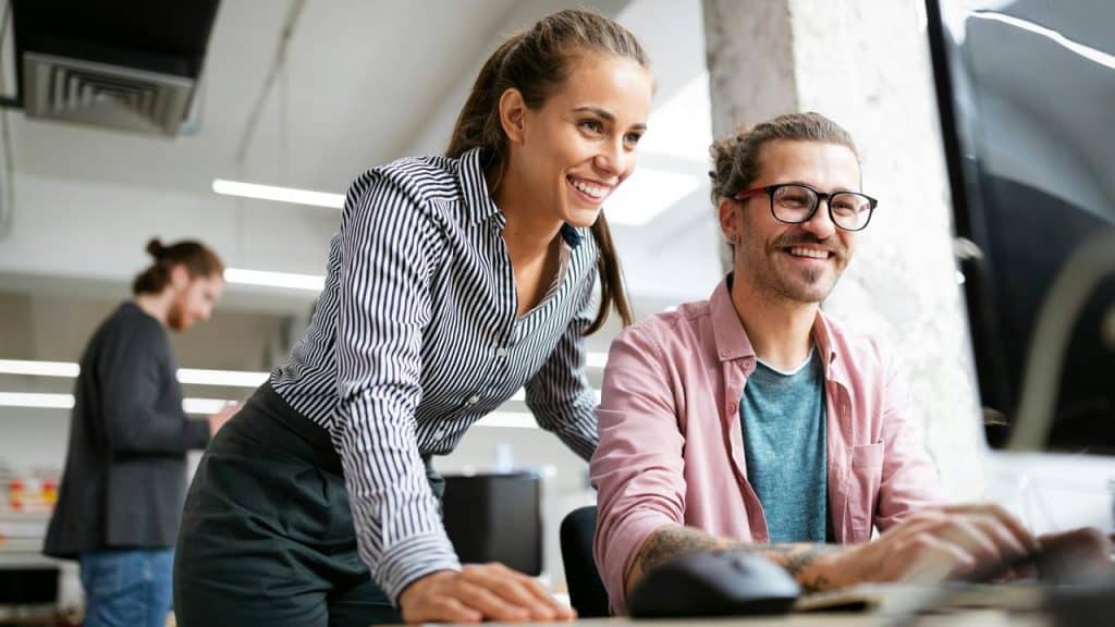 A woman and man smile while working together at a computer.