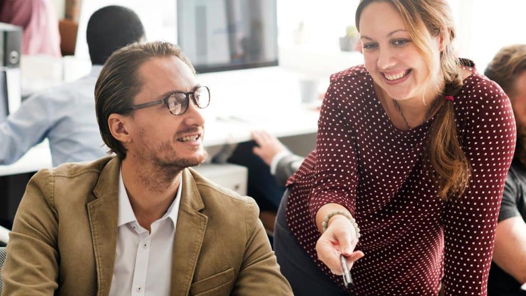 A woman smiles while showing something to a man in an office.