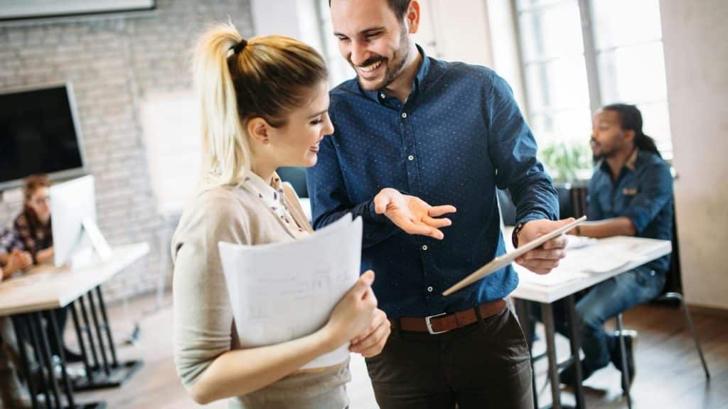 A man and woman smile while discussing papers in an office.