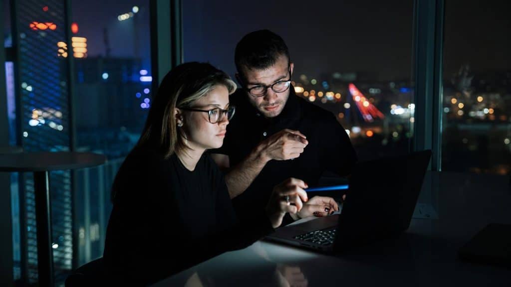 A man and woman work on a laptop together at night.