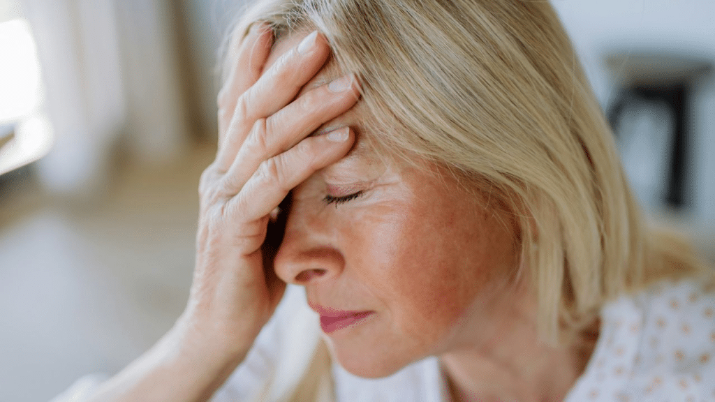 A middle-aged woman with blonde hair holds her hand to her forehead, looking stressed.