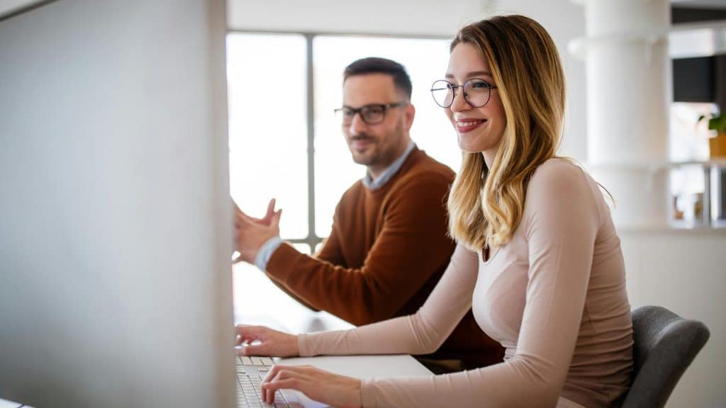 A woman smiles while working on a computer next to a colleague.