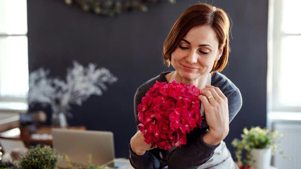 A woman smiles while holding a bouquet of pink flowers.