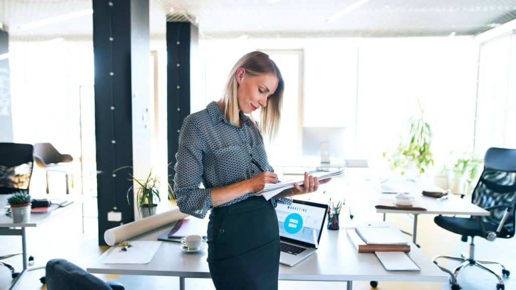 A woman writes in a notebook while standing in a bright office.