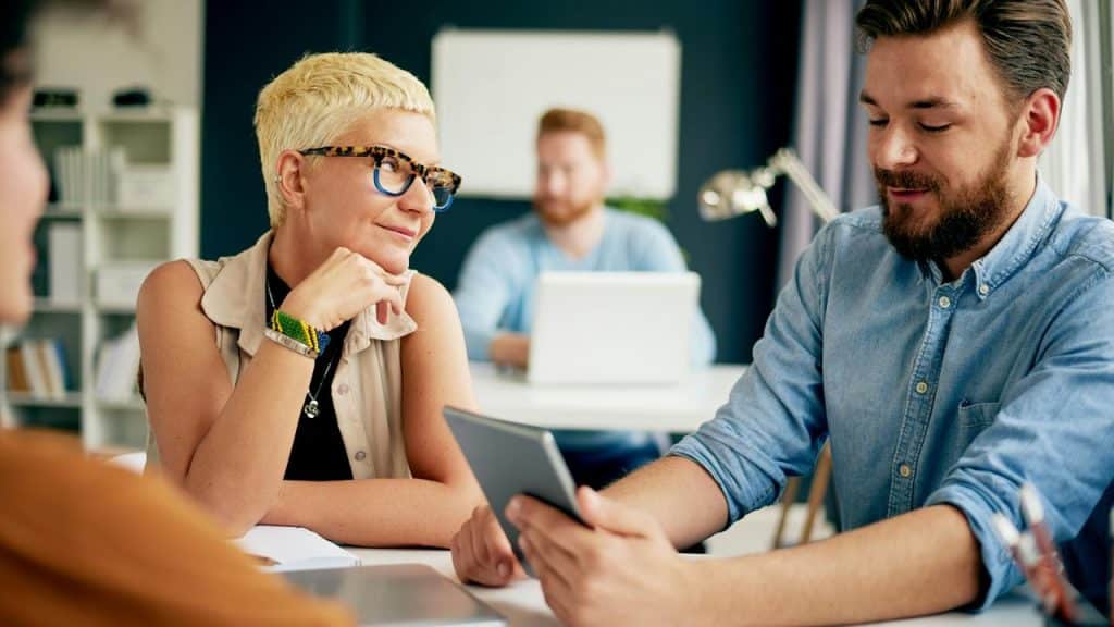 A man shows a tablet to a woman during a meeting in an office.