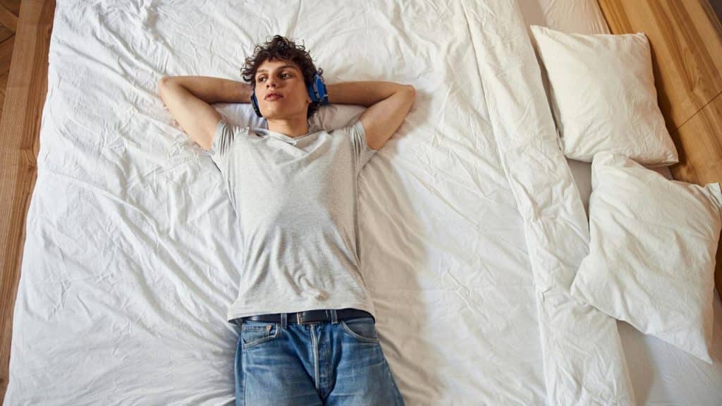 A young man lying on a bed wearing headphones.