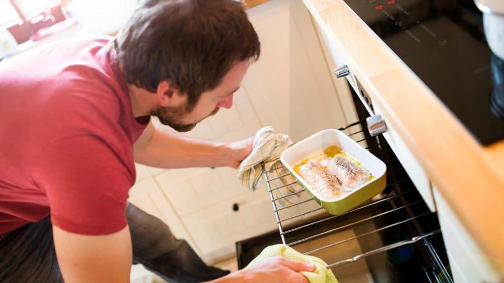 A man placing a dish with fish into an oven.