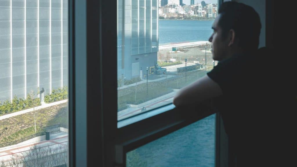 A man leaning on a window ledge looking out at the city and river.