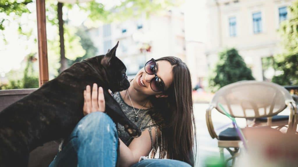 A woman wearing sunglasses smiling while holding a black dog outdoors.