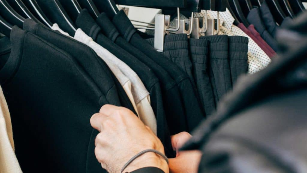A person browsing black clothes on a clothing rack.