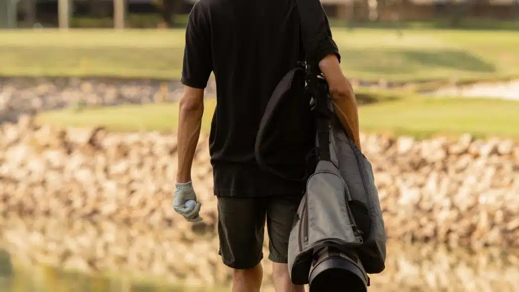 A golfer carrying a bag while walking on a golf course.