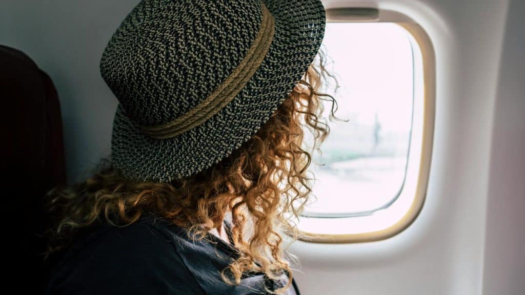 A woman wearing a hat looking out of an airplane window.