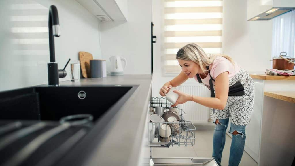 A woman loading cups into a dishwasher in a modern kitchen.