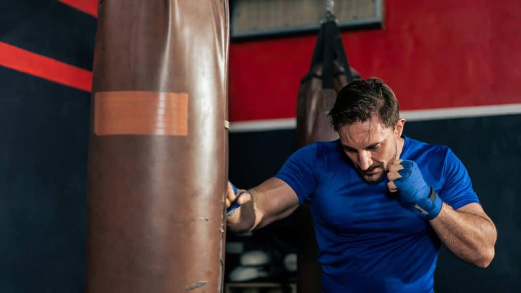 A man in a blue shirt training with a punching bag.
