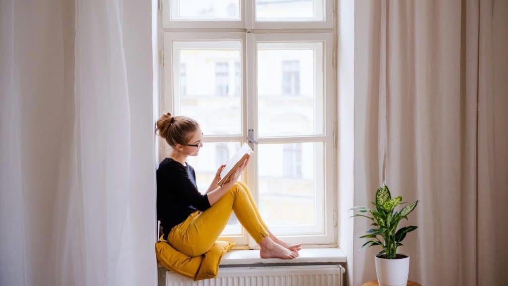 A woman sitting on a windowsill reading a book.