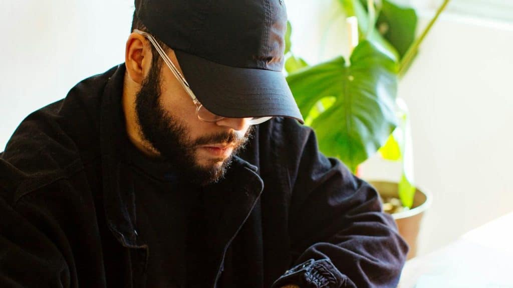 A man wearing a black cap and glasses looking down indoors.