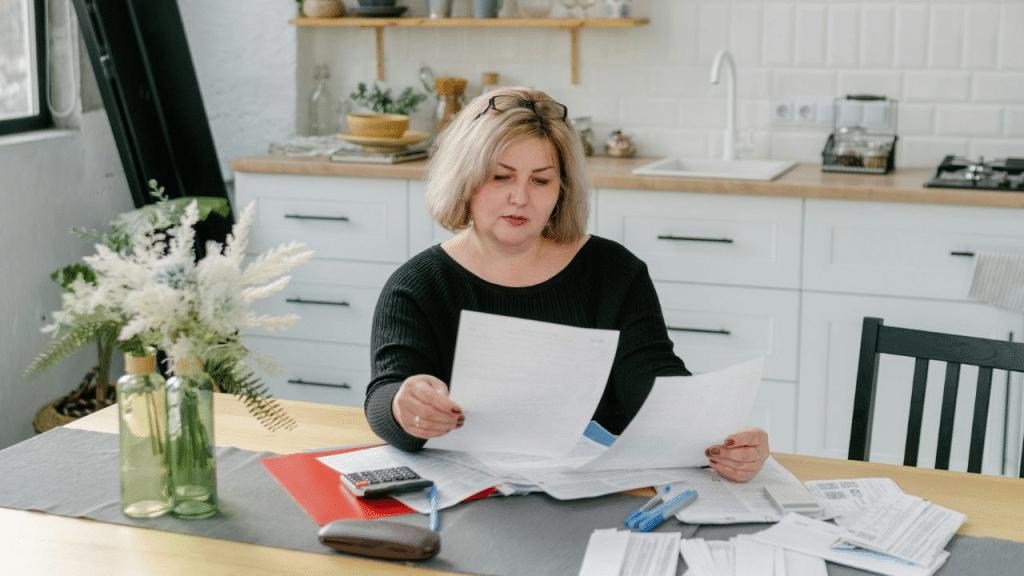 A focused woman in a black shirt is reviewing documents at a kitchen table.
