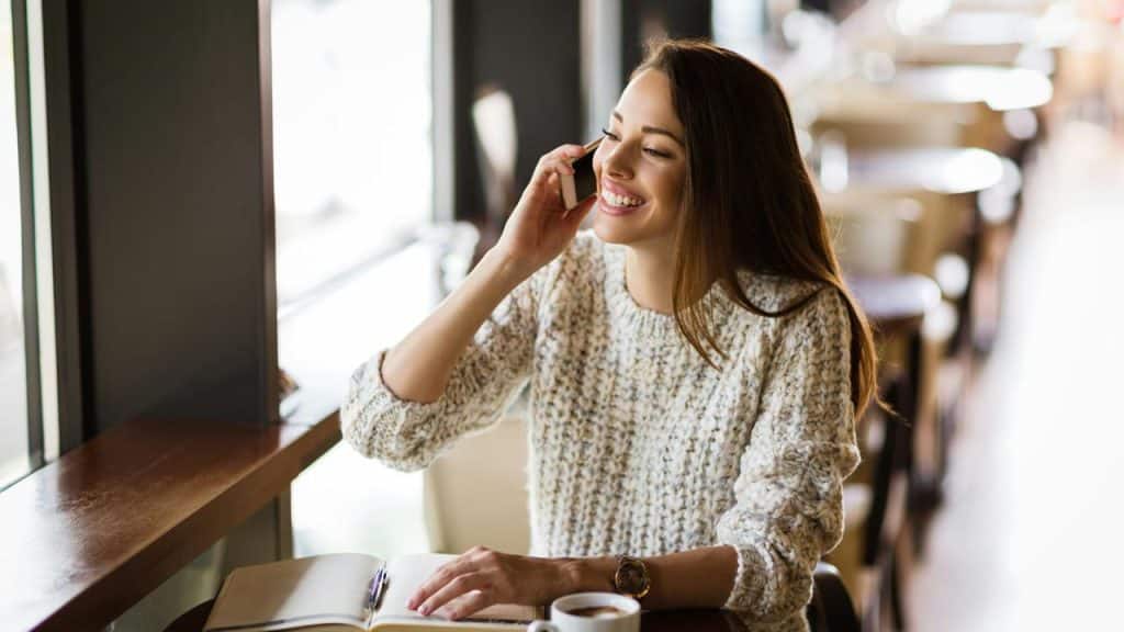 A woman smiling while talking on the phone in a café.