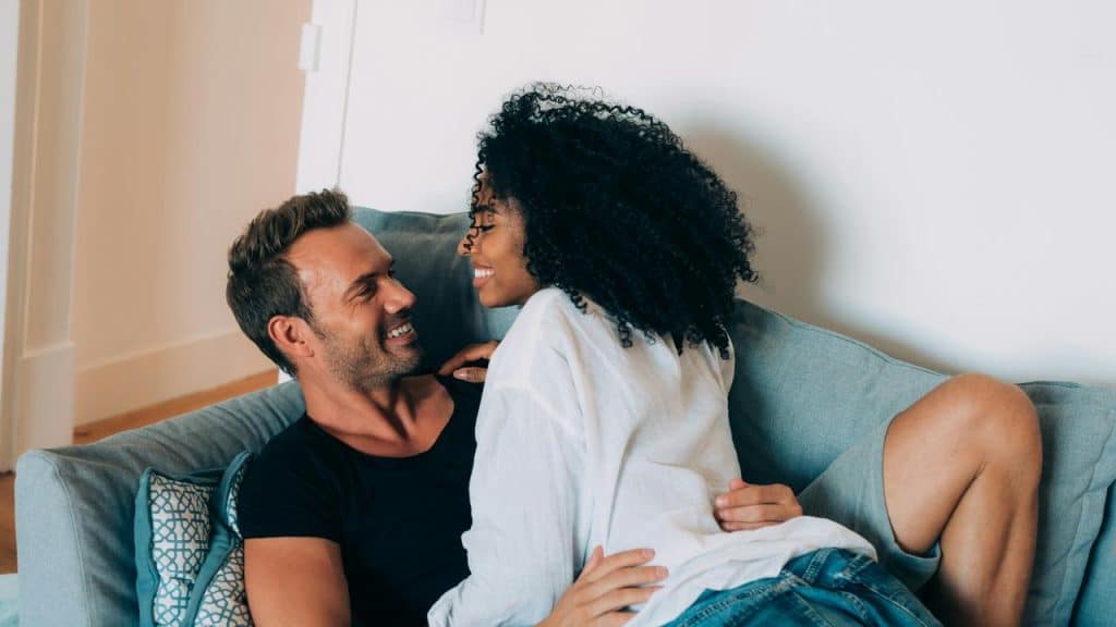 A couple smiling and cuddling together on a couch.