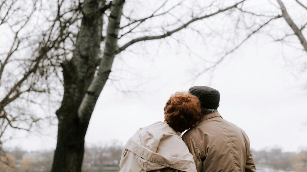 A senior couple sitting closely together outdoors on a cloudy day.