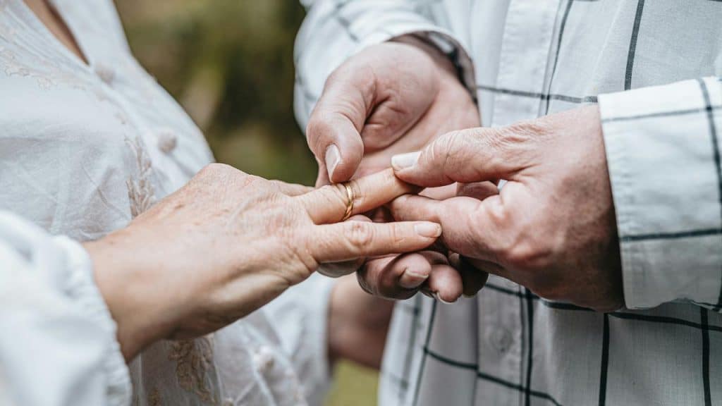 A close-up of an elderly couple holding hands while one places a ring on the other's finger.