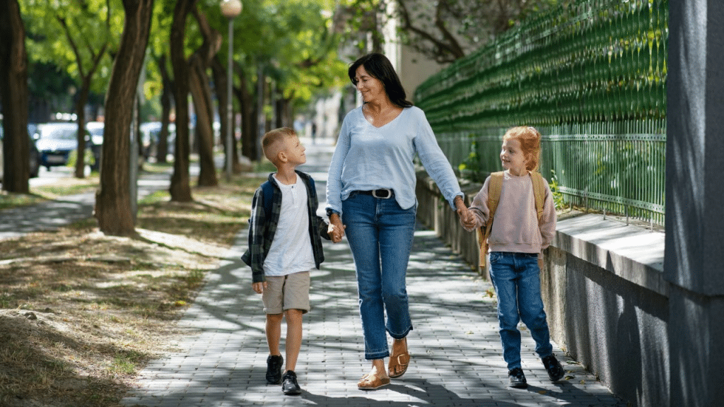 A happy mother holding hands with her two children as they walk on a sidewalk.