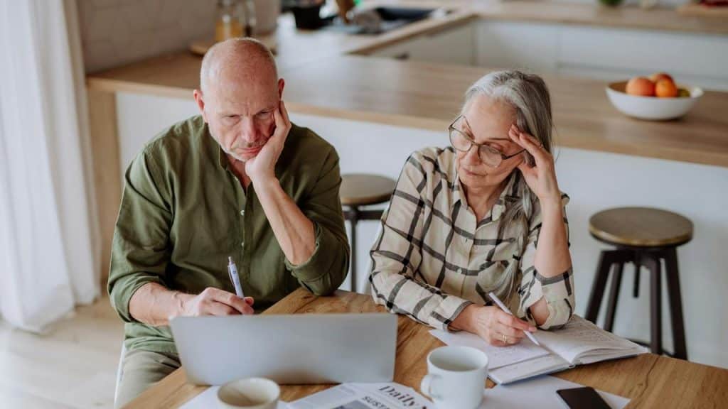 An elderly couple sitting at a table looking concerned.