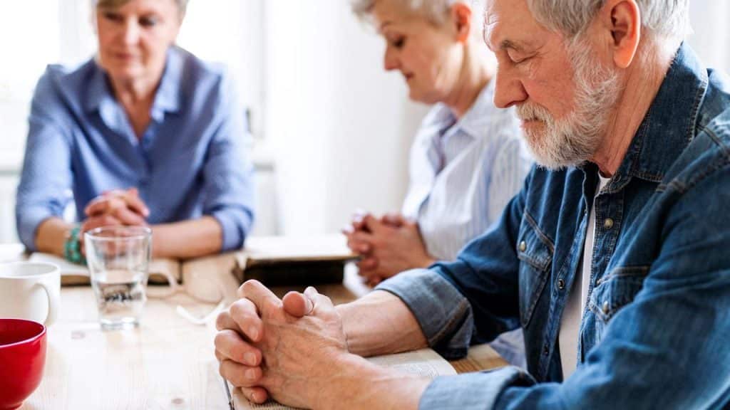 A group of elderly people sitting at a table and praying together.