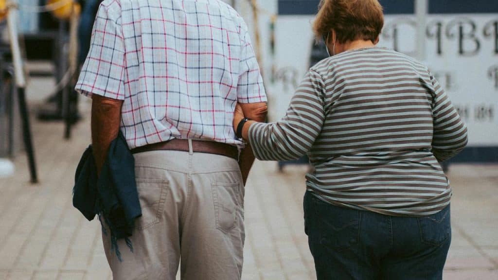 An elderly couple walking together while holding each other’s arms.