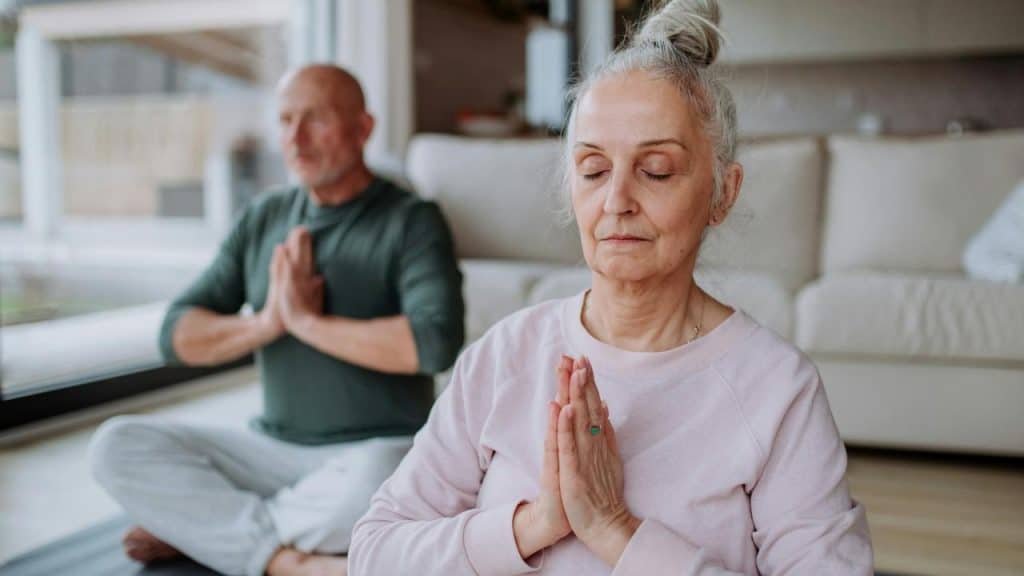 An elderly couple practicing yoga together indoors.
